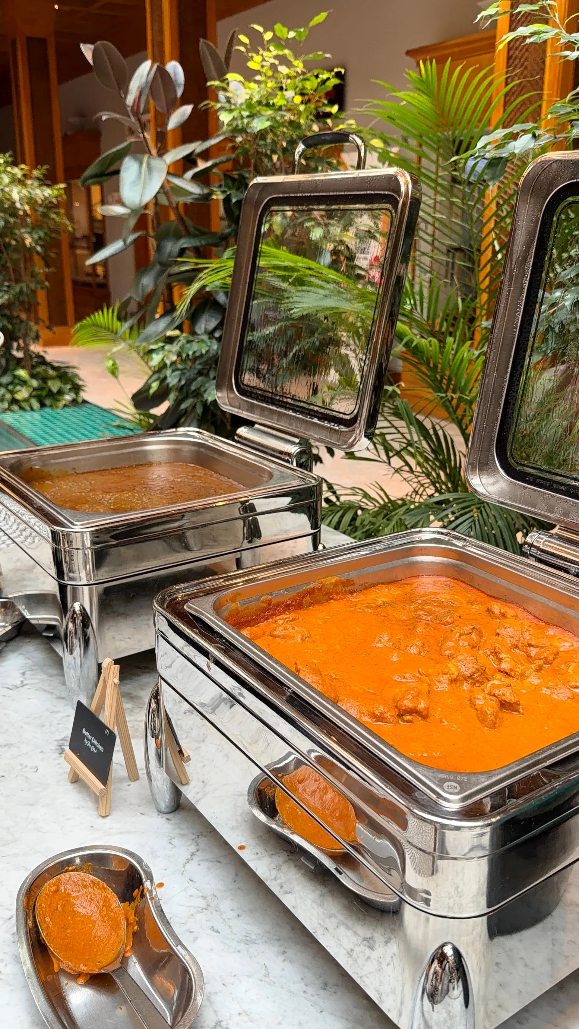 Stainless-steel chafing dishes of butter chicken and curry at an elegant Indian catering buffet (illustrative photo)