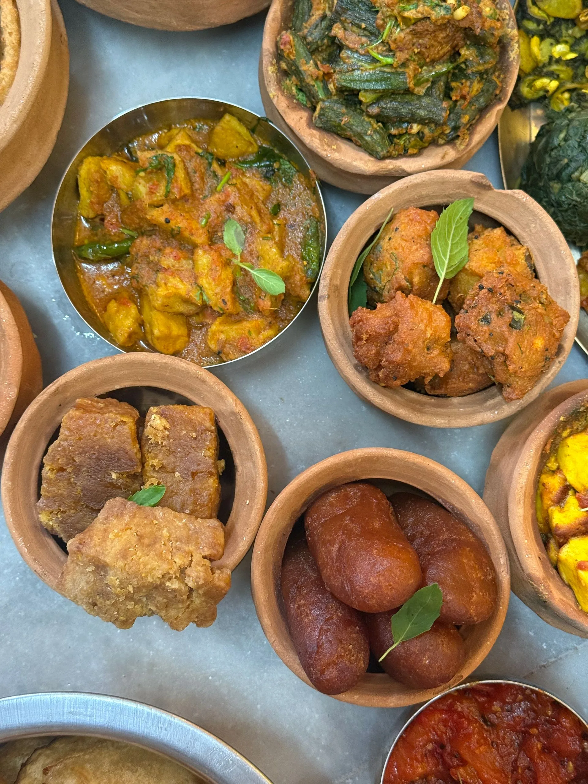 Overhead Indian catering spread with curries, pakoras and gulab jamun in clay handis (illustrative photo)